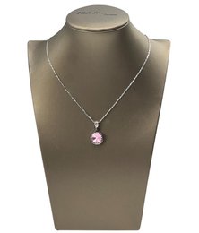 A round, pink gemstone pendant on a gold chain necklace.