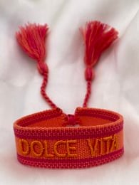 Colorful festival bracelet with tassels and text. Woven bracelet in red and orange with "Dolce Vita" text. Woven bracelet in gray with "Love Story" text.