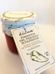 Organic piquillo peppers in a jar, with a label indicating they are roasted and peeled. The peppers appear to be a deep red color and are arranged on a striped plate.