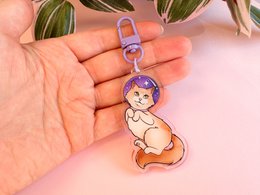 Cute ragdoll cat astronaut keychain with a whimsical design featuring a cartoon-style astronaut cat in a purple and orange color scheme.