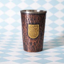 Hammered copper beer mug with gold crest emblem, suitable for serving beer or other beverages.