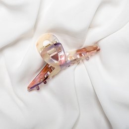 A pink plastic hair claw clip with a twisted design. The clip is made of a translucent pink material and has a simple, minimalist style.