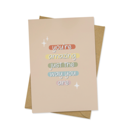 A greeting card with a simple, colorful design and the text "You're amazing just the way you are" written on it. The card appears to be made of beige cardstock and has a minimalist, whimsical aesthetic.