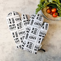 A pair of black and white patterned oven mitts with a tribal or mudcloth-inspired design. The mitts are made of a durable, heat-resistant material and are suitable for use in the kitchen when handling hot dishes or pans.