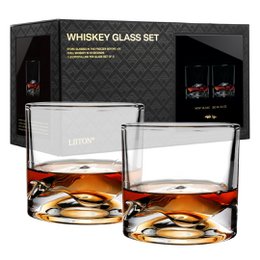 Two clear glass whiskey glasses containing amber-colored liquid and ice cubes. The glasses have a simple, elegant design.