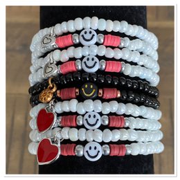 A stack of colorful beaded bracelets featuring white beads, red accents, and various charms including hearts and smiley faces.