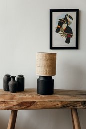 Chic black bedside lamp with rattan shade, providing warm, ambient lighting for a cozy, modern bedroom.