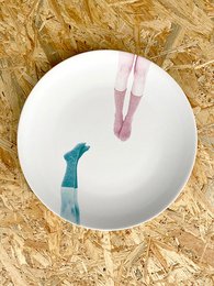 A round white plate with pink and green legs, suitable for use as a decorative wall plate or light fixture.