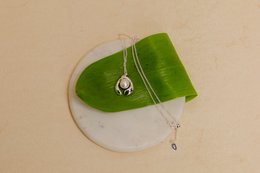 A delicate pearl necklace pendant on a green leaf. The necklace is displayed in a white jewelry box.