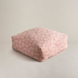 A large, square, pink pouf with a geometric pattern. The pouf appears to be made of a soft, textured fabric and has a plush, cushioned design.
