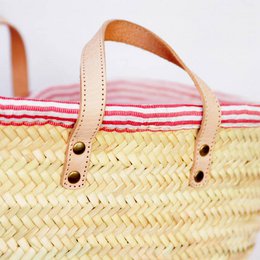 Woven straw basket with red and white striped fabric lining and leather handles. Suitable for picnics or beach trips.