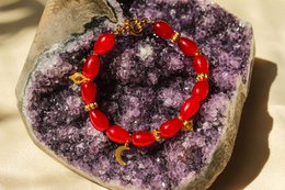 Vibrant red beaded bracelet with a circular design, featuring a mix of round and oval-shaped beads against a backdrop of natural amethyst geode.