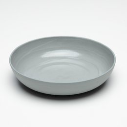 A round, shallow bowl made of stucco material in matte grey, matte white, soft yellow, or dark brown colors. The bowl has a simple, minimalist design with a spiral pattern in the center.