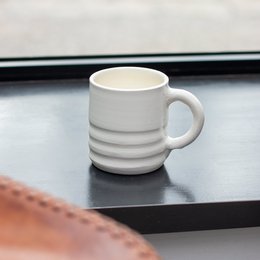 A white ceramic mug with a simple, minimalist design featuring horizontal ridges or grooves around the body of the cup.