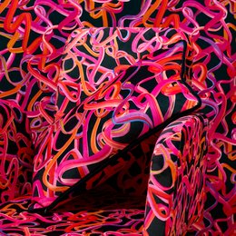Vibrant, abstract cushion with bold, swirling patterns in shades of pink, red, and black. The cushion has a rectangular shape and appears to be made of a soft, textured material.