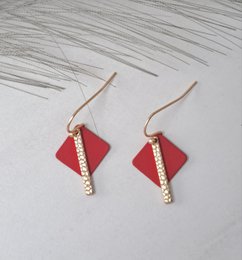 Matte gold-toned earrings with a bold red diamond-shaped pendant and a row of sparkling crystals along the edge, creating a statement look.