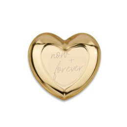Small heart-shaped gold bowl with the text "now + forever" engraved on it, surrounded by crumpled paper and dried flowers.
