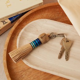  A leather tassel keyring with a peace symbol engraved on it, featuring a wooden keychain with blue and white striped accents.