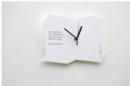 A small white analog watch with a simple, minimalist design. The watch face features a clean, text-based design with no numbers or other decorative elements.
