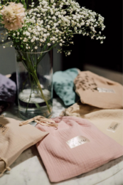 A cozy, feminine arrangement featuring a glass vase filled with delicate white flowers, a soft pink sweater, and a pair of slippers on a marble surface.