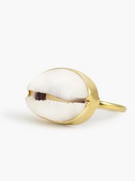 A gold-toned ring featuring a single cowrie shell as the centerpiece. The ring has a simple, minimalist design that showcases the natural beauty of the shell.