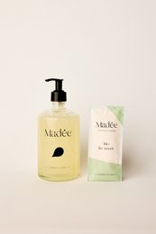 Glass hand soap set with a natural, earthy scent. Features a clear glass bottle with a black pump dispenser. Includes two bars of hand soap in a light green color.