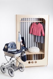 A children's wardrobe with a pink sweater and a vintage-style baby stroller. The wardrobe has a striped pattern and wooden accents, suitable for a nursery or child's bedroom.