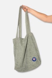 A large, light green tote bag made of soft, textured material with a circular logo patch on the front.