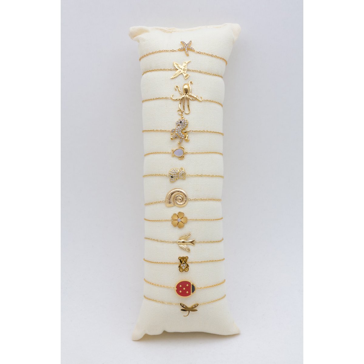 Présentoir coussin en tissu écru comprenant un lot de 12 bracelets fins en maille forçat dorée déjà installés.
