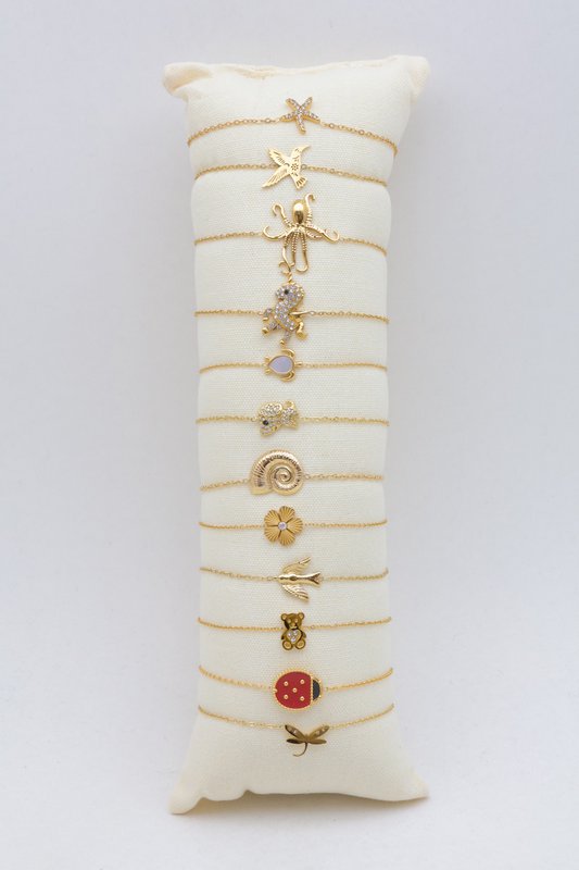 Présentoir coussin en tissu écru comprenant un lot de 12 bracelets fins en maille forçat dorée déjà installés.