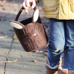 A brown felt Easter egg basket with a bunny design, a handle, and a pom-pom. The basket is handcrafted in Nepal and is a fair trade product suitable for an Easter egg hunt or as a children's Easter decoration.