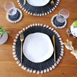 Seagrass placemat set with light blue color and cowrie shell accents. Circular shape with woven texture and natural fiber materials.