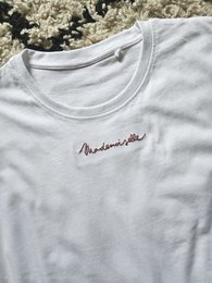 White t-shirt with 'Mademoiselle' embroidered text, available in sizes S, M, L, XL.