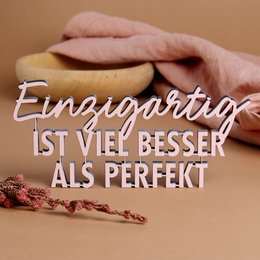 A unique, decorative statue featuring the German text "Einzigartig ist viel besser als perfekt" which translates to "Unique is much better than perfect". The statue has a minimalist, modern design with a pink and white color scheme, and appears to be made of a durable material like resin or ceramic.