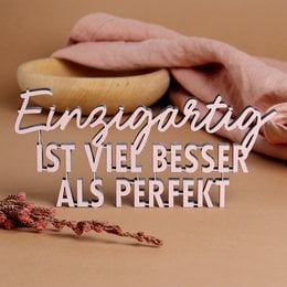 A unique, decorative statue featuring the German text "Einzigartig ist viel besser als perfekt" which translates to "Unique is much better than perfect". The statue has a minimalist, modern design with a pink and white color scheme, and appears to be made of a durable material like resin or ceramic.