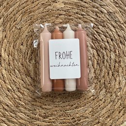 A set of cozy, colored candles in shades of pink and white, arranged on a woven straw mat. The candles have a festive, holiday-inspired appearance, suitable for use during the Christmas season.