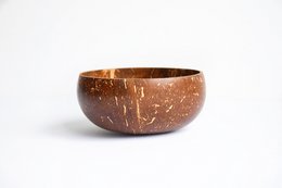 A medium-sized coconut bowl with a natural, rustic appearance. The bowl has a round, shallow shape and is made from coconut shell material.