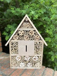 Wooden insect hotel with multiple compartments for housing beneficial insects in the garden. Features a triangular roof design and natural wood finish.
