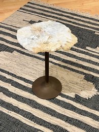  A white, round side table with a natural stone top on a striped rug.
