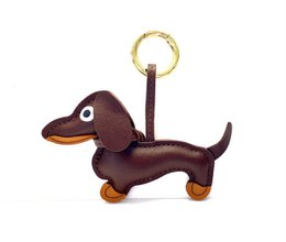 Dachshund-shaped keychain in dark brown and gold colors. Made of leather material with a gold-tone metal ring for attaching to keys or bags.
