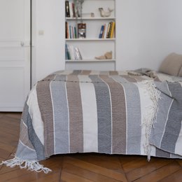 Pacana Blanket - A cozy, striped throw blanket made of soft, natural materials. The blanket features a neutral color palette of grays and whites, creating a warm and inviting look for any living space.