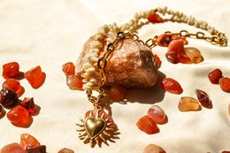 A gold-toned charm necklace with a round, textured pendant and dangling amber-colored stones.