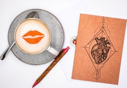 A ceramic mug with an anatomical heart design and a red lipstick kiss print.