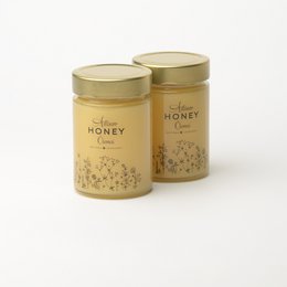 Blossom honey, a natural and pure honey product available in various sizes. The honey is packaged in glass jars with gold lids, showcasing its high quality and natural appearance.