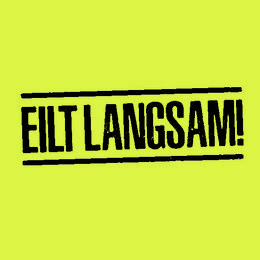 Sticky notepad with text "EILT LANGSAM!" (Hurry slowly!) in bold black text on a bright yellow background.