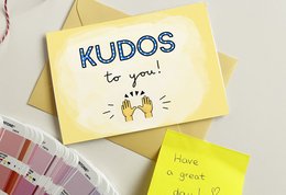 A yellow greeting card with the text "KUDOS to you!" and a hand-drawn illustration of a thumbs-up gesture. The card appears to be a simple, cheerful design meant to convey appreciation or praise.