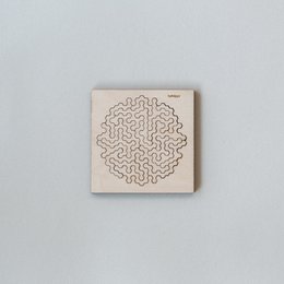A wooden puzzle with a complex maze-like pattern on a light-colored background. The puzzle appears to be a challenging brain teaser or logic game.