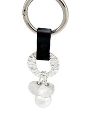  A silver-toned metal keychain with a black leather strap and a decorative charm featuring a round metal disc and two pearl-like beads.