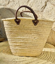 Woven straw basket bag with brown leather short handles, natural tan color, reinforced tote style handbag.