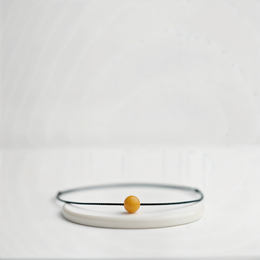 Minimalist beaded bracelet with a single yellow bead on a thin black cord.